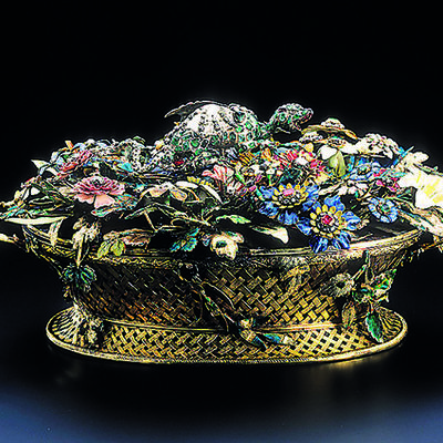 Ein goldener, filifgraner Korb gefüllt mit verschiedenen, fein ausgearbeiteten, bunten Blumen und Blüten, teilweise mit Edelsteinen besetzt.